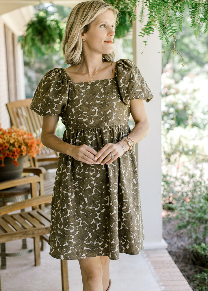 Model wearing a khaki babydoll dress with brown floral, square neck, bubble short sleeves.