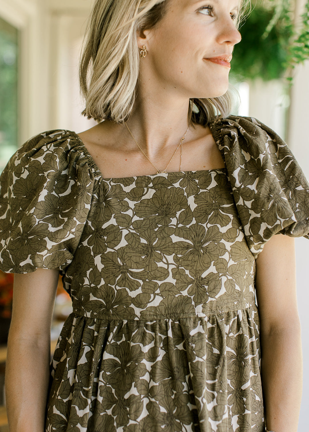 Close up of square neckline and bubble short sleeves on a khaki babydoll dress with brown floral. 