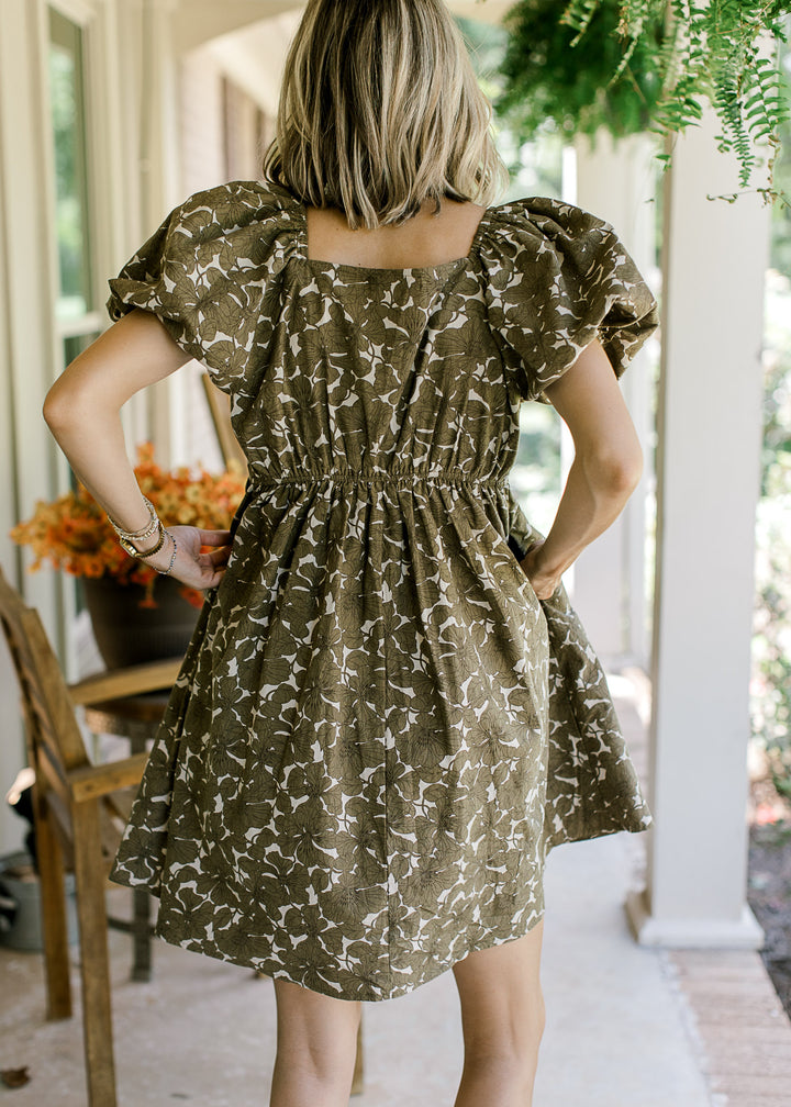 Back view of Model wearing a khaki dress with brown floral, square neck, bubble short sleeves.