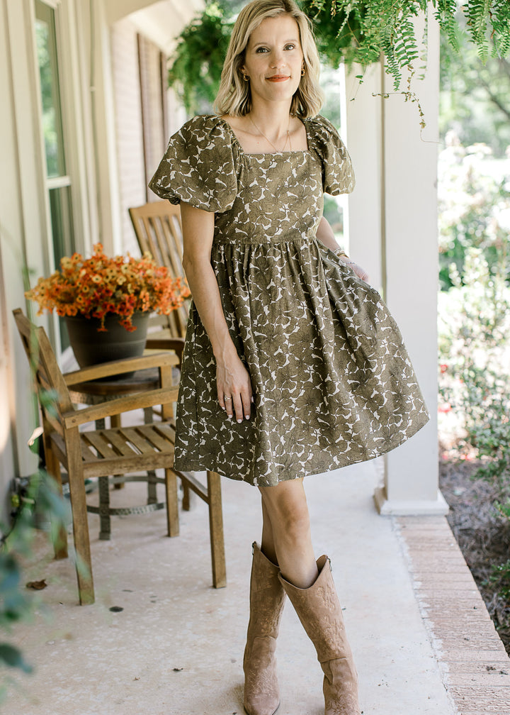 Model wearing boots and a khaki babydoll dress with brown floral, square neck, bubble short sleeves.