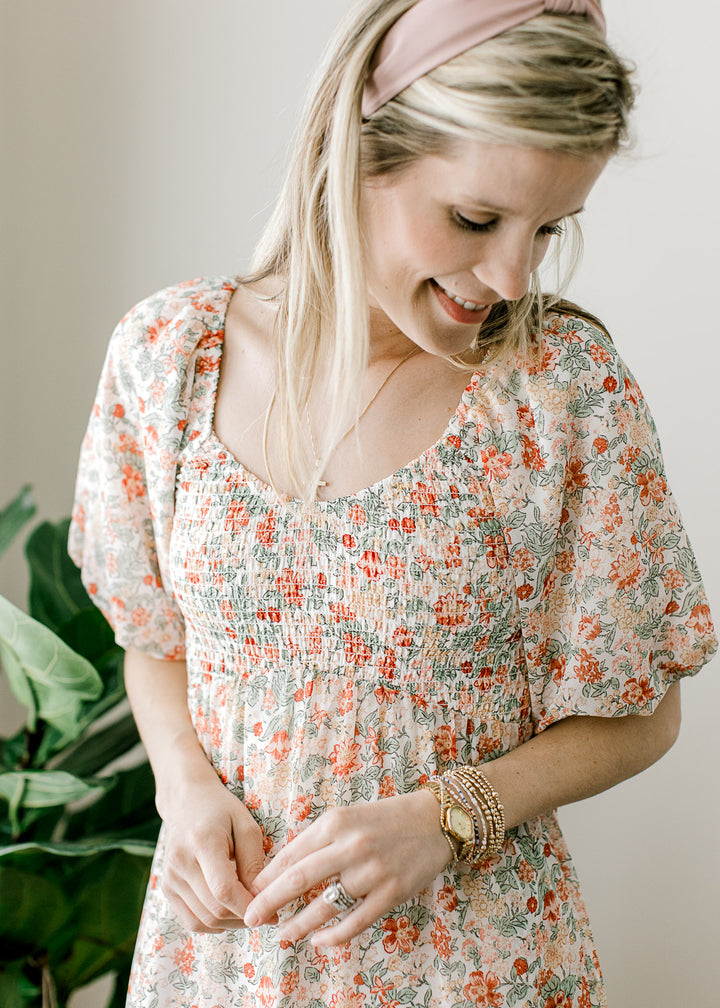 Close up of v-neck, smocked bodice and bubble short sleeves on an off white midi with floral. 