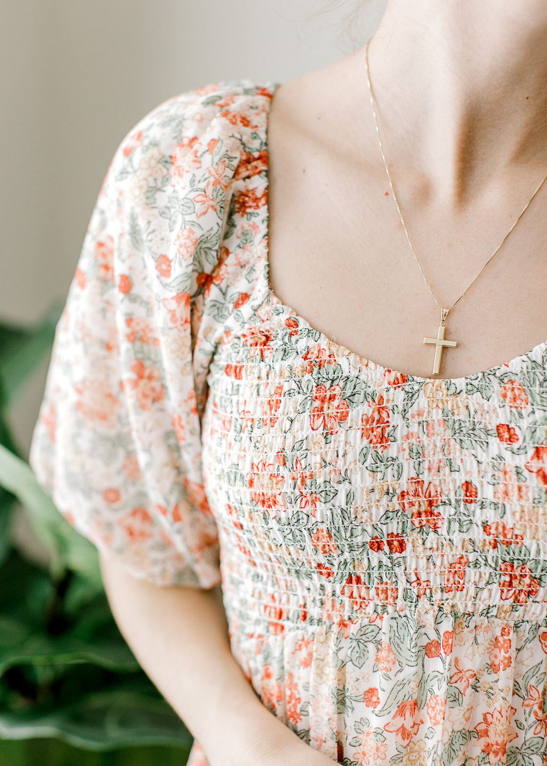 Close up o smocked bodice and elastic along the shoulder of an off white midi with floral. 