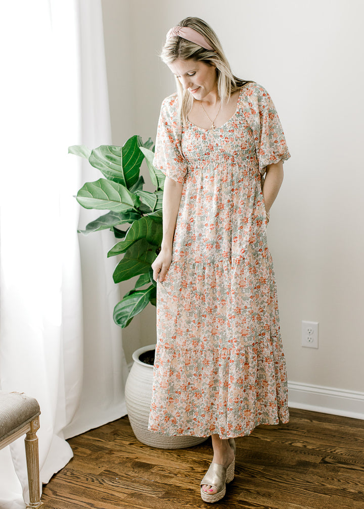 Model wearing an off white midi with peach floral, pockets and a v-neckline wiht smocked bodice.