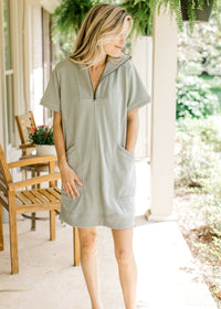 Model wearing a mossy green dress with short sleeves, patch pockets and a quarter zip closure. 