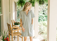 Model wearing a mossy green dress with short sleeves, patch pockets and a ribbed detail. 