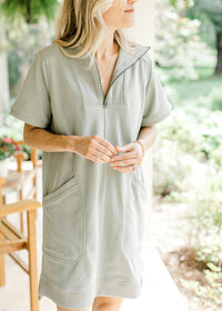 Model wearing a mossy green above the knee dress with patch pockets and a quarter zipper. 