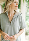 Close up of mock neck and quarter zip on a short sleeve mossy green above the knee dress. 