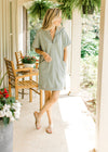 Model wearing sandals and a mossy green dress with short sleeves, patch pockets and zip closure. 
