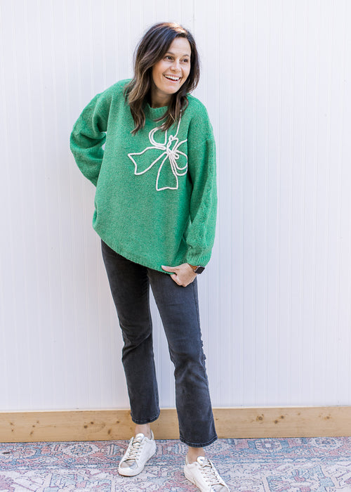 Model wearing a bright green sweater with a raised white bow outline and long sleeves.