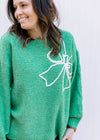 Model wearing a bright green sweater with a raised white bow outline and a round neck.