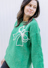 Close up of raised white bow on a bright green sweater with long sleeves and a round neck.