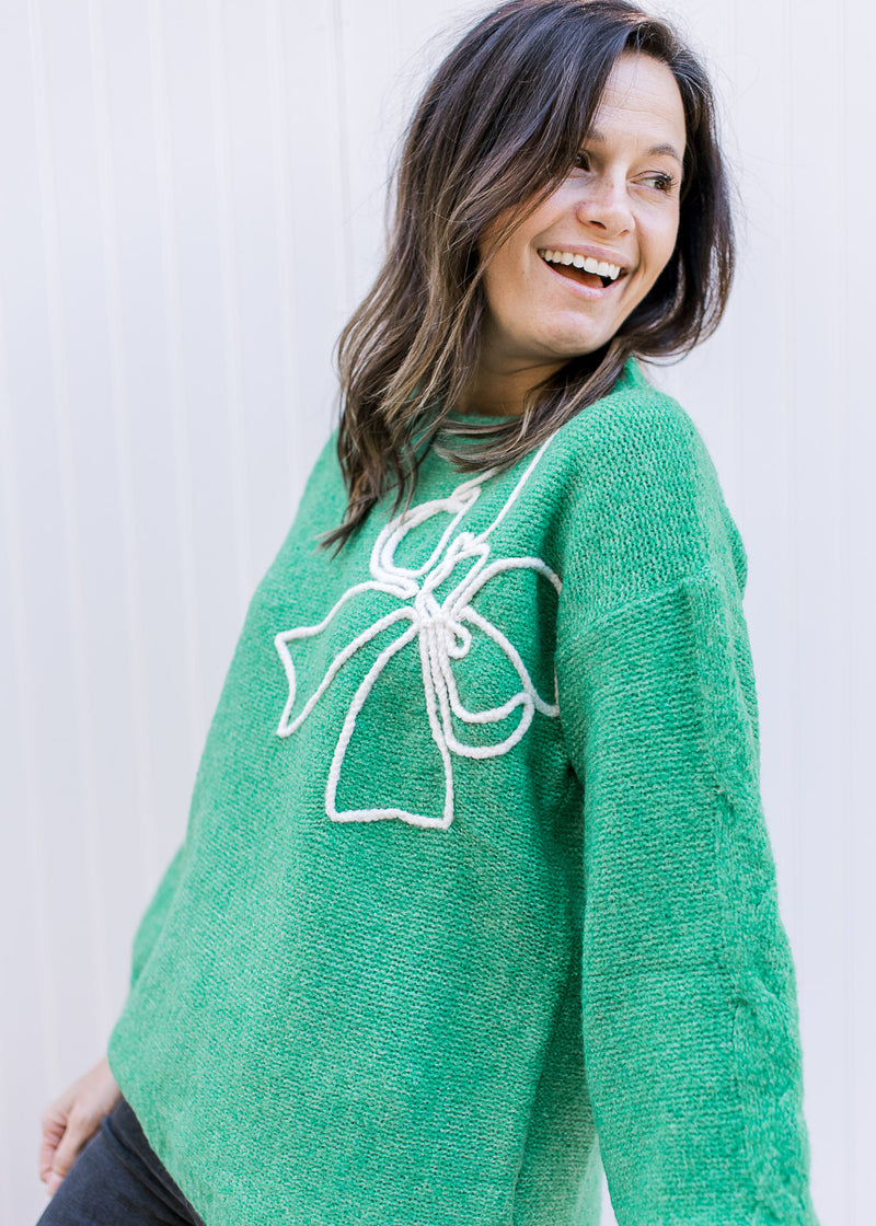 Model wearing a classic bright green sweater with a raised white bow outline and long sleeves.