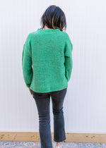 Back view of Model wearing a bright green sweater with a raised white bow outline.