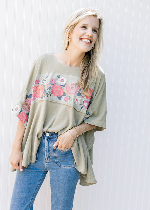 Model wearing a sage top with a floral design, split sides and short sleeves. 