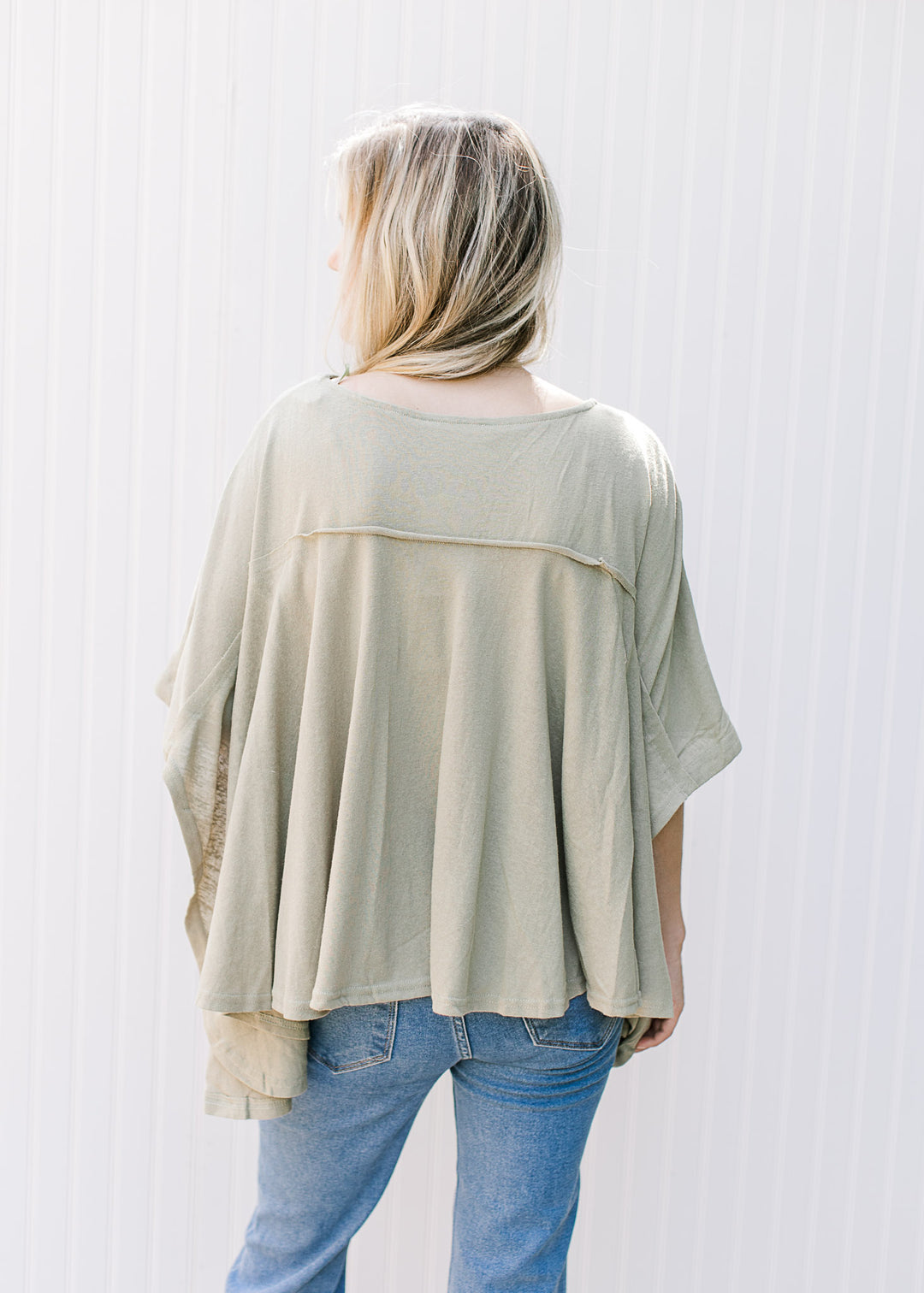 Back view of Model wearing a sage top with a floral design, split sides and short sleeves. 