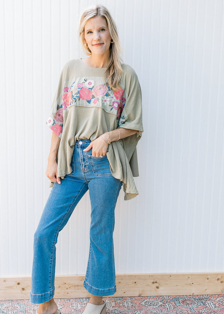 Model wearing jeans with a sage top with a floral design, split sides and short sleeves. 