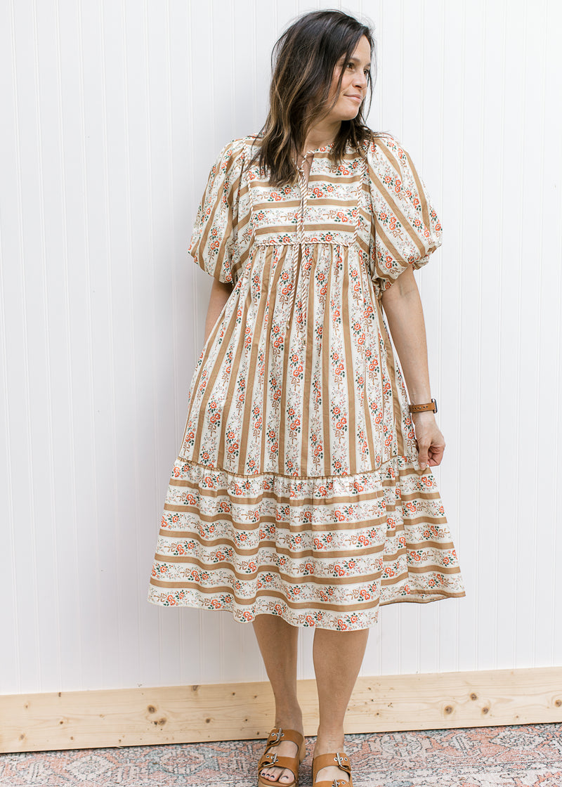 Model wearing a cream midi with short sleeves and alternating golden stripes and floral. 