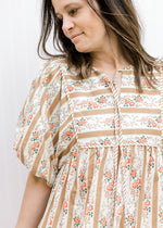 Close up of bubble short sleeves and v-neck with a tie on a cream and gold striped dress. 