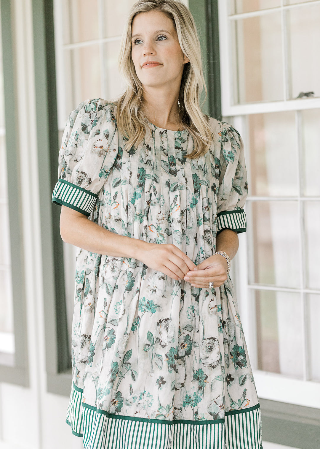 Model wearing a grayish tan above the knees dress with green floral, round neck and short sleeves. 