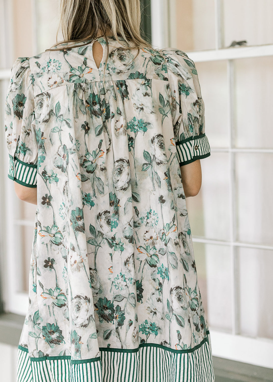 Model wearing a grayish dress with green floral a green and white stripe detail at cuff and hem.