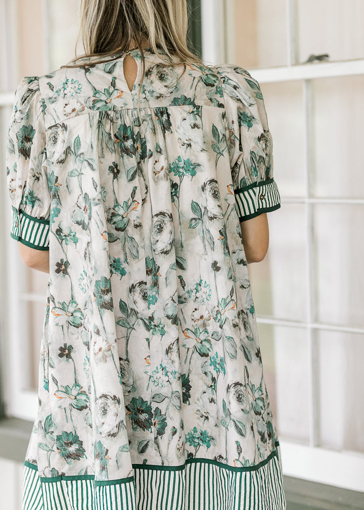 Model wearing a grayish dress with green floral a green and white stripe detail at cuff and hem.