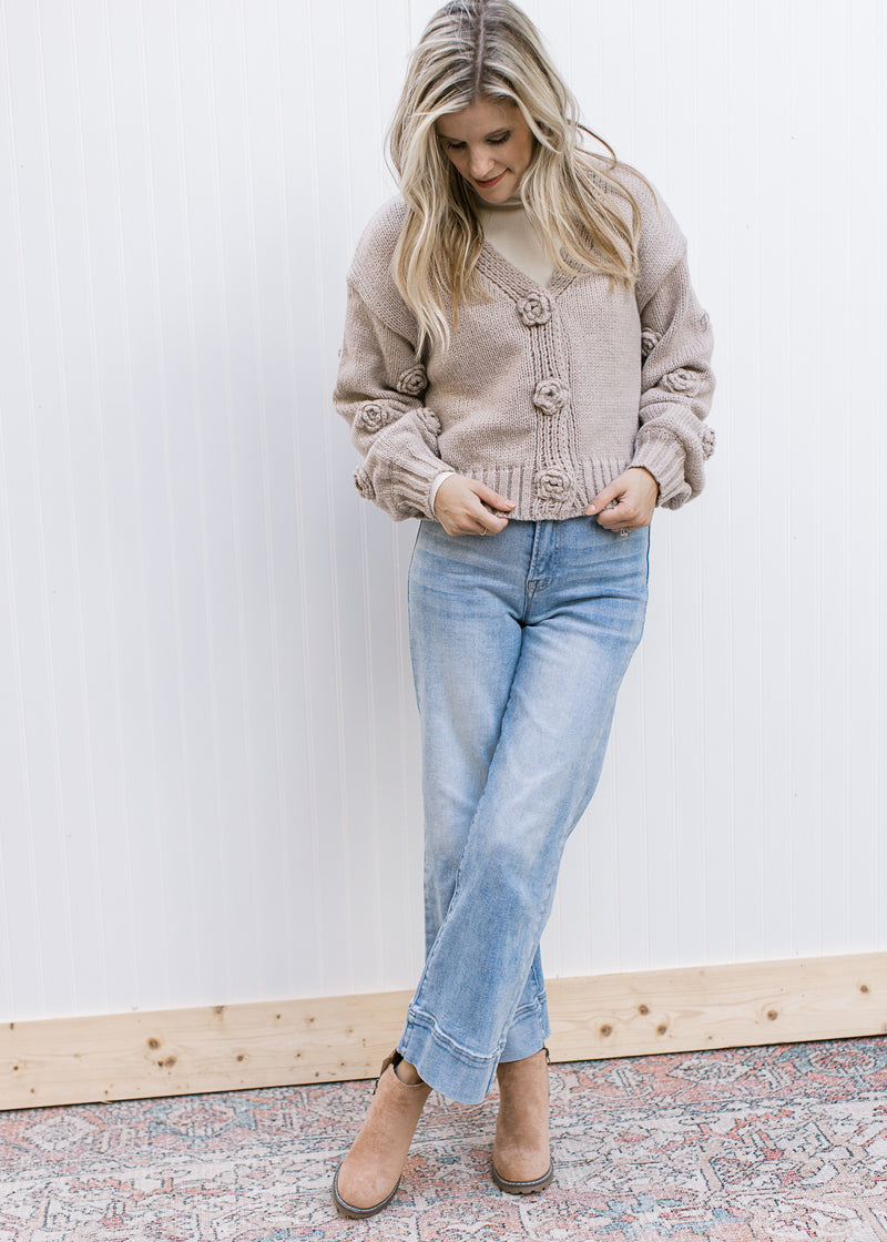 Model wearing jeans and booties with an oatmeal colored knit cardigan with floral knit flowers.