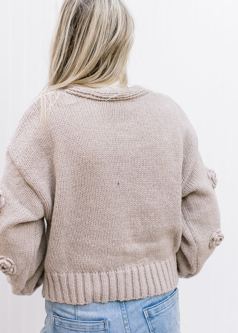 Back view of Model wearing an oatmeal colored knit cardigan with floral knit flowers. 