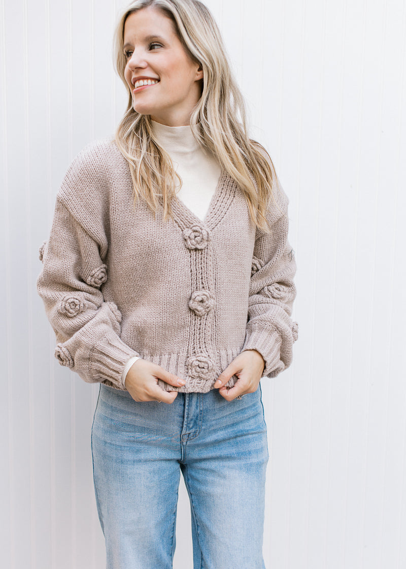 Model wearing an oatmeal colored knit cardigan with 3 snap buttons with floral knit flowers. 