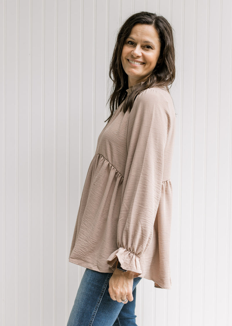 Side view of Model wearing a beige top with poet long sleeves and a round neck with a ruffle.