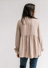 Back view of Model wearing a beige top with poet long sleeves and a round neck with a ruffle.