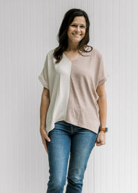 Model wearing jeans with a cream and tan two-toned v-neck top with short sleeves. 
