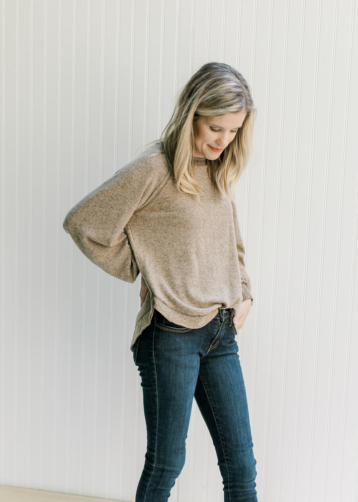 Model wearing a light brown top with a round neck, long sleeves and exposed hem.