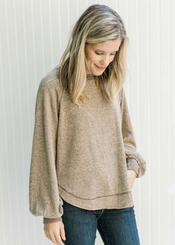 Model wearing jeans with a light brown top with long sleeves and ribbing at the cuff and neck. 