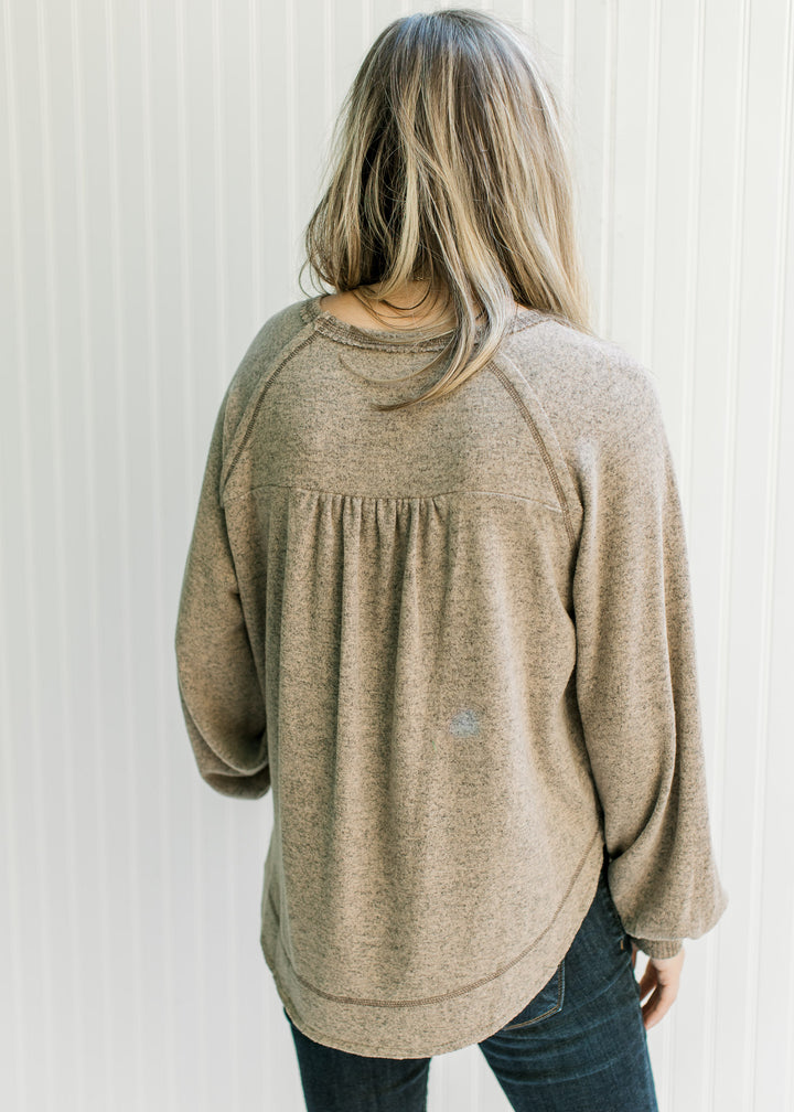 Back view of Model wearing a light brown top with long sleeves and ribbing at the cuff and neck. 