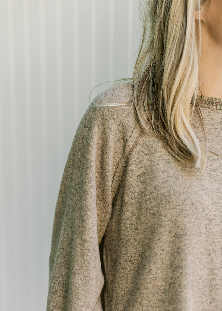 Close up of exposed hem and ribbed round neck on a light brown sweater with long sleeves. 