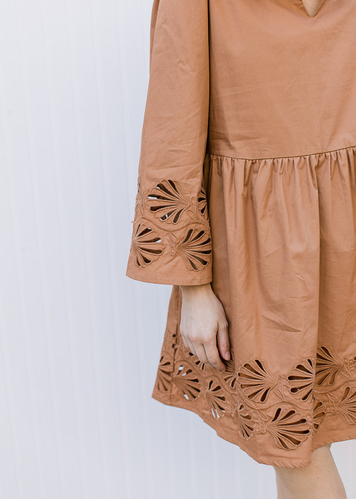 Close up of lace floral cut out at hem and cuff of a toffee babydoll dress with 3/4 sleeves. 