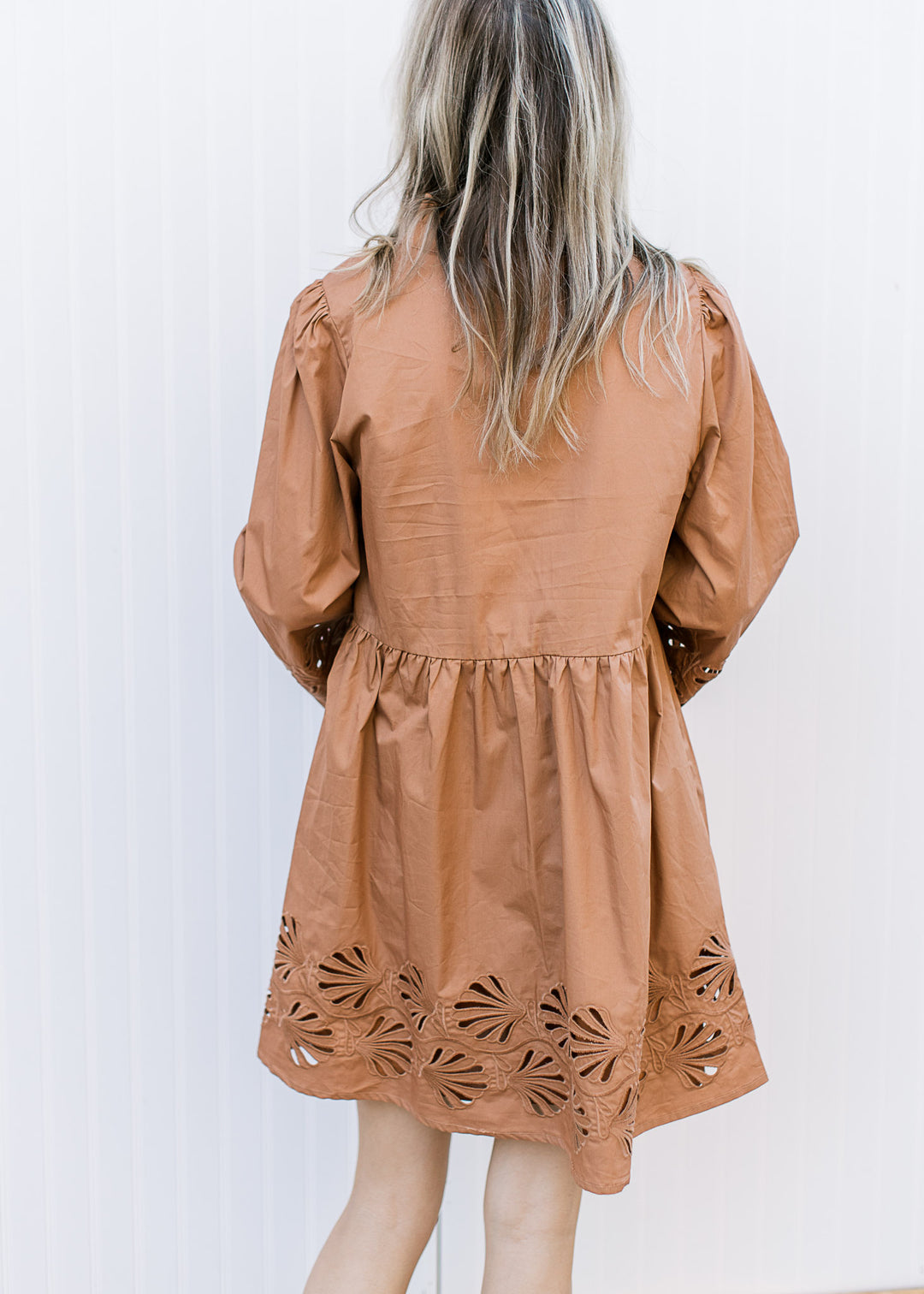 Back view of Model wearing a toffee babydoll dress with a floral lace cutout and 3/4 sleeves.