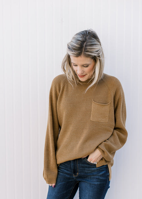 Model wearing a toffee color, knit sweater with a patch pocket, long sleeve and a round neck.