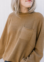 Close up of patch pocket on a toffee colored sweater with long sleeves and a round neck.