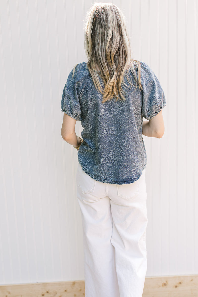 Back view of Model wearing a blue top with floral pattern, short sleeves and button front.