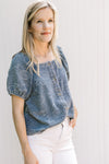 Model wearing a blue top with floral pattern, short sleeves square neck and button front. 