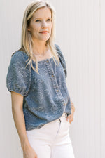 Model wearing a blue top with floral pattern, short sleeves square neck and button front. 