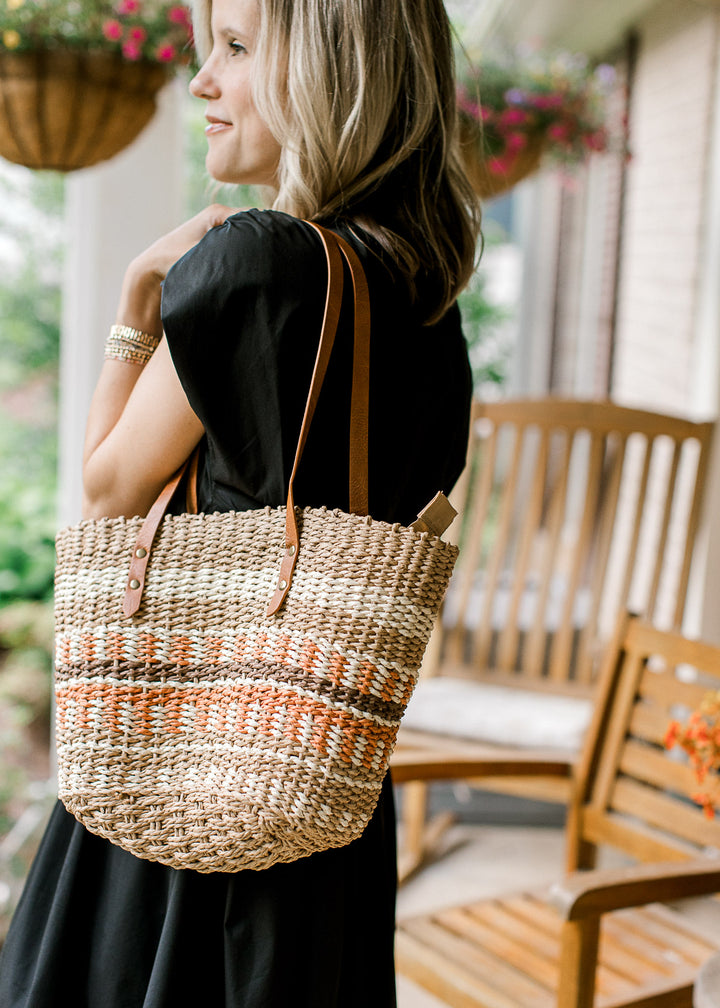 Model holding a woven straw purse with taupe, cream, brown, and rust pattern and faux leather strap.