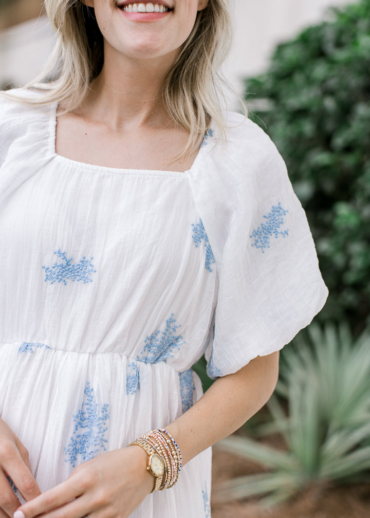 Close up of square neck, elastic waist and bubble short sleeves on a white midi with blue floral. 
