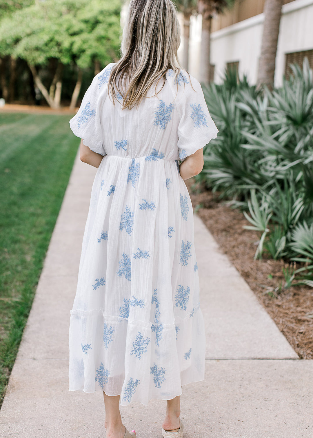 Back view of Model wearing a white midi with pale blue flowers, square neck and short sleeves.