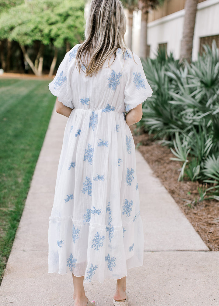 Back view of Model wearing a white midi with pale blue flowers, square neck and short sleeves.