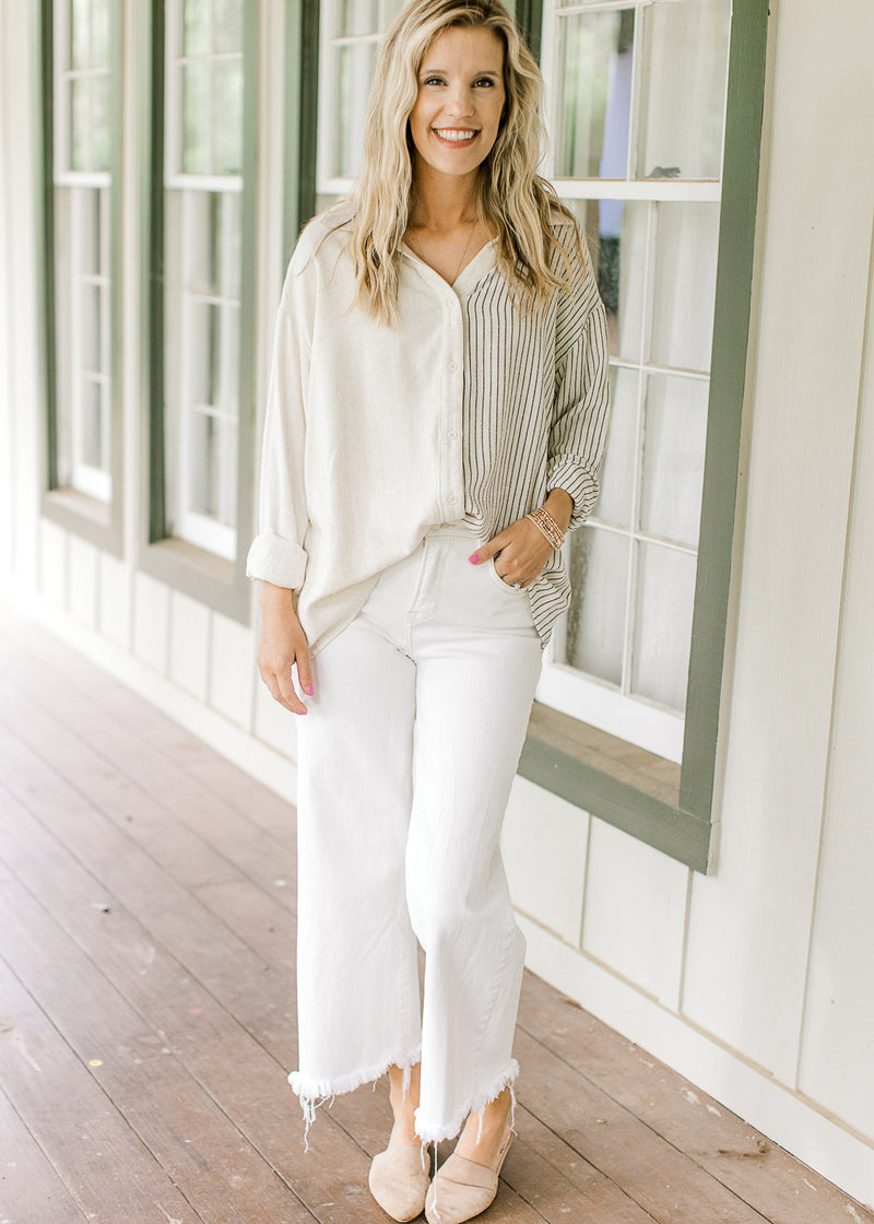 Model wearing mule, white pants and a button down top with one side cream and one side navy stripes.