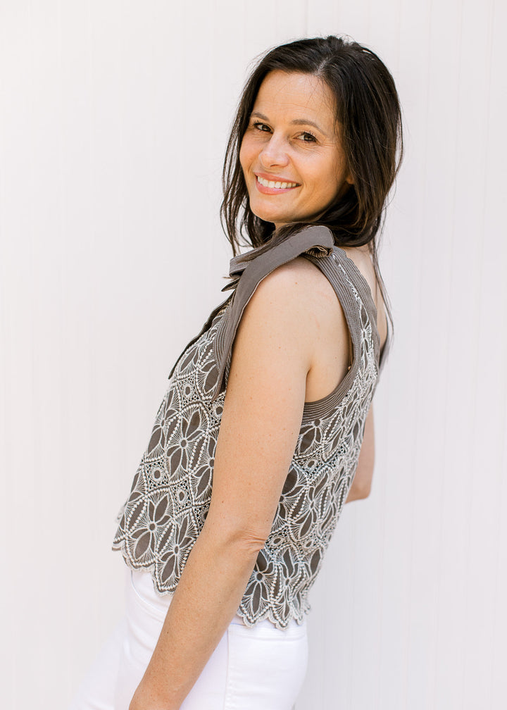 Model wearing a mocha top with cream floral embroidery, faux tie straps and a scalloped hem.
