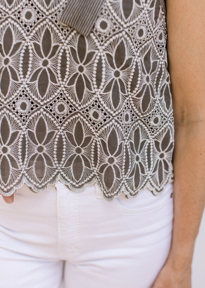 Close up of scalloped hem on a mocha sleeveless top with cream floral embroidery. 