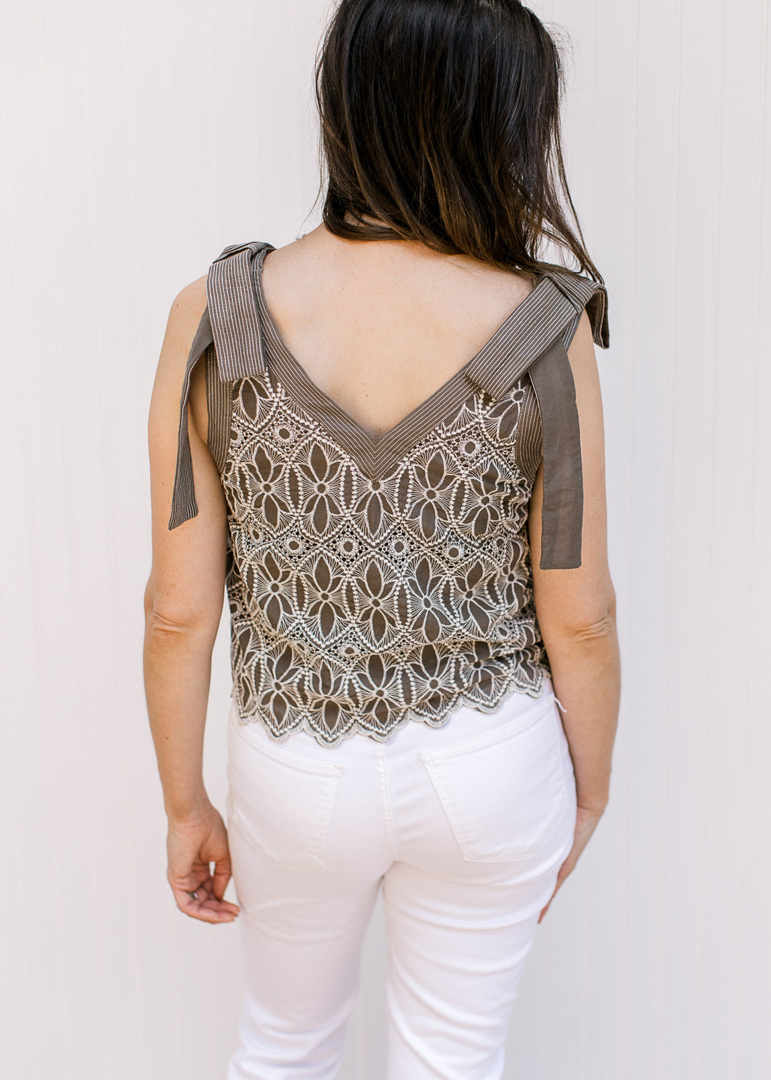 Back view of Model wearing a mocha v-neck top with cream floral embroidery, faux tie straps. 